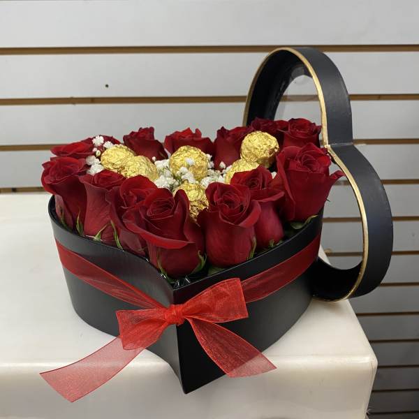 Heart-shaped black box of red roses with gold-wrapped chocolates and a red ribbon bow