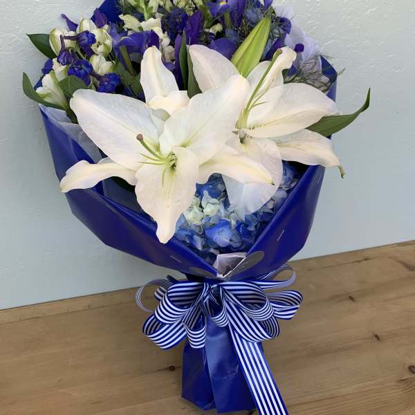 Bouquet of white lilies and blue flowers wrapped in blue paper with a striped ribbon.