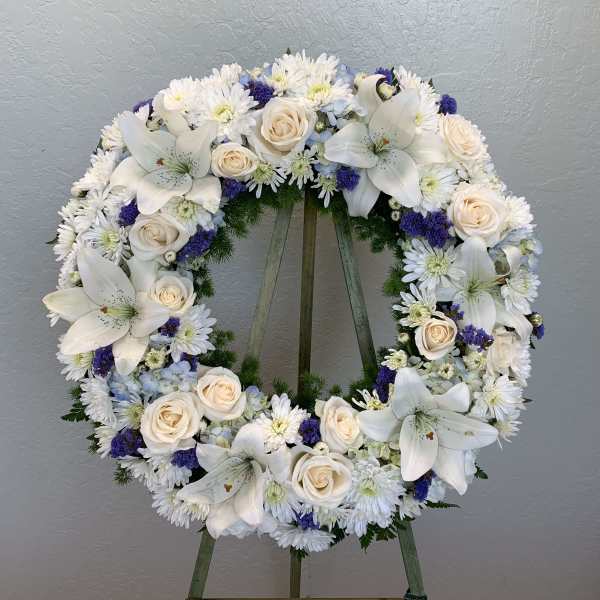 Circular floral wreath with white lilies, cream roses, and white daisies on an easel