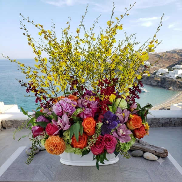 Large mixed flower arrangement in a white container with yellow branching blooms