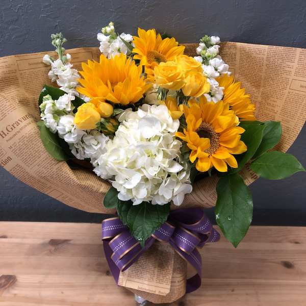 Bouquet of yellow sunflowers, white hydrangeas, and yellow roses wrapped in paper