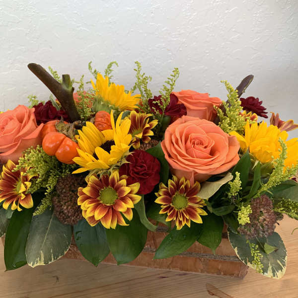 Autumn floral arrangement with roses, daisies, and small pumpkins in a low container