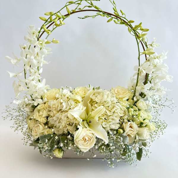 White floral basket arrangement with roses and orchids on an arched handle