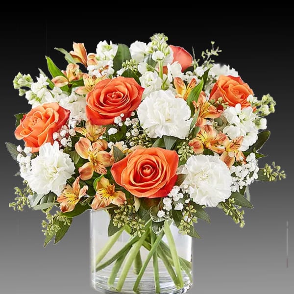 Orange roses and white carnations in a clear glass vase