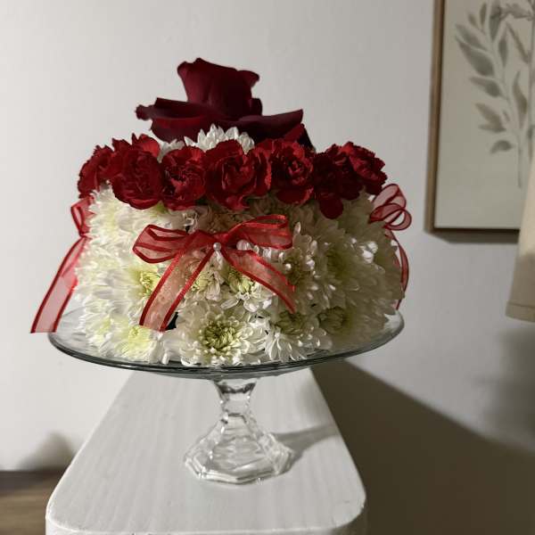 Red and white floral arrangement in a glass pedestal bowl with ribbon
