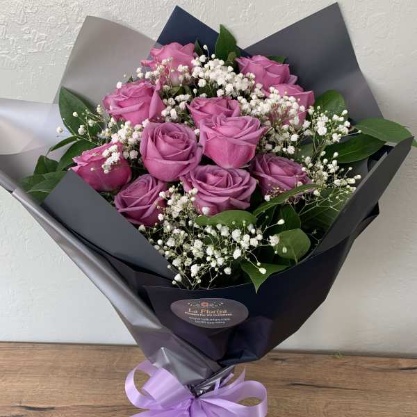 Bouquet of pink roses with white baby's breath in dark wrapping
