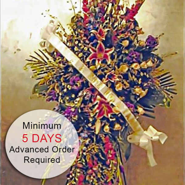 Tall standing spray of mixed red, purple, and yellow flowers with a white ribbon across the front