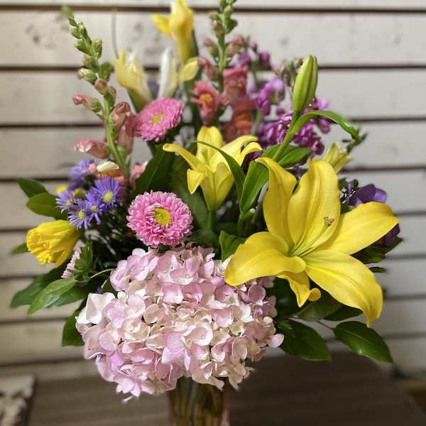 Mixed bouquet with yellow lilies, pink hydrangea, and purple flowers in a glass vase