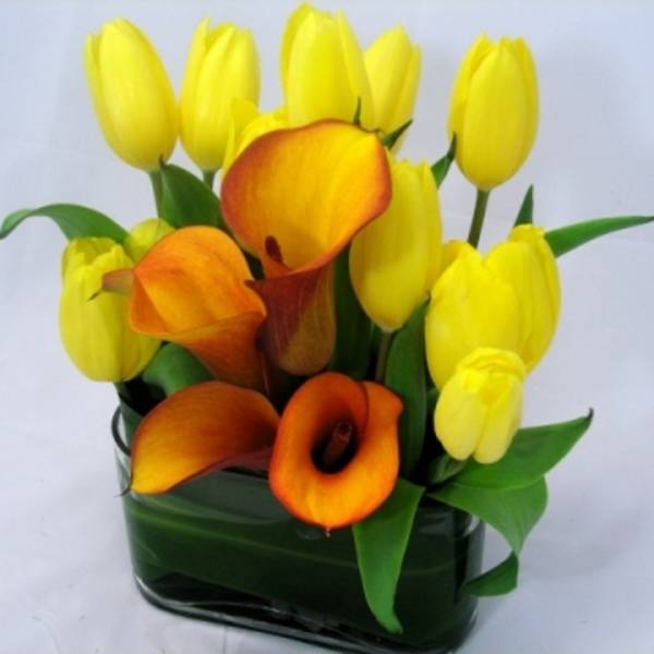 Yellow tulips and orange calla lilies in a dark glass vase