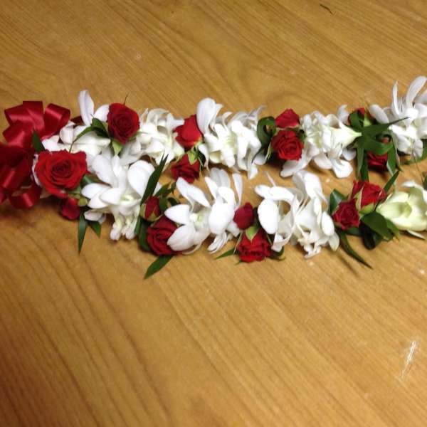 Red and white floral lei with ribbon on a wooden surface