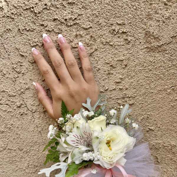 Small white floral wrist corsage with pink ribbon and tulle