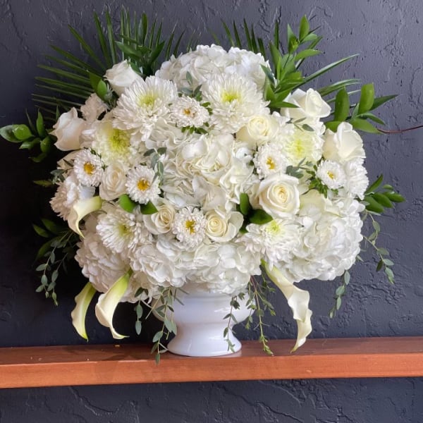 White floral arrangement in a white vase with roses and mums