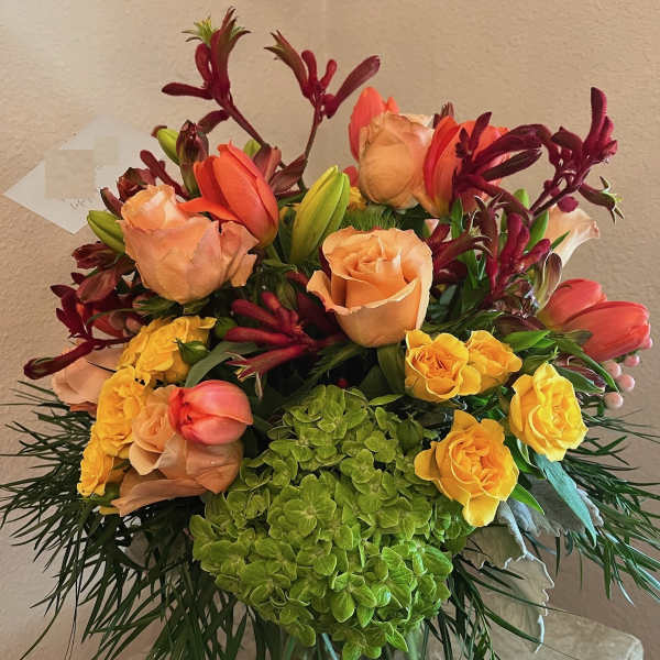 Mixed bouquet of peach roses, yellow roses, and red tulips in a glass vase