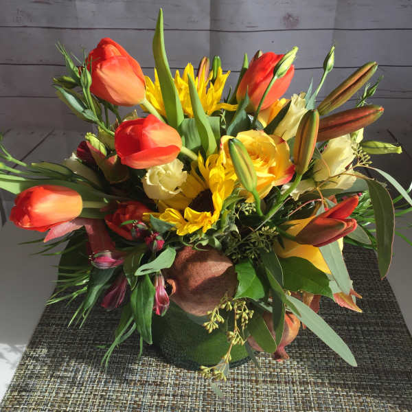 Bouquet of orange tulips, yellow sunflowers, and lilies in a low arrangement