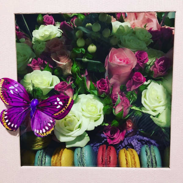 Boxed arrangement of pink and white roses with a purple butterfly and colorful macarons
