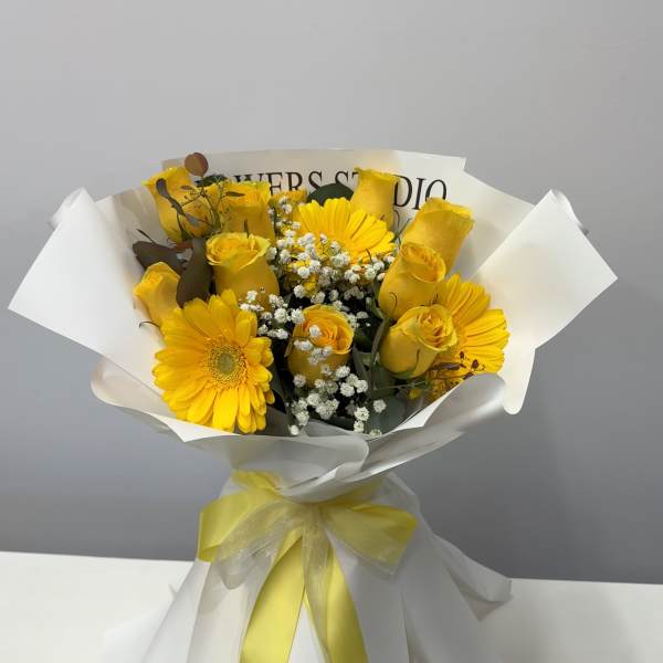 Yellow roses and gerbera daisies wrapped in white paper with a yellow ribbon