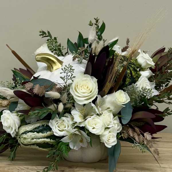 White roses and lilies in a low beige container with dried accents