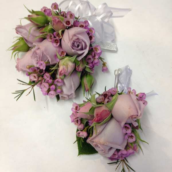 Two lavender rose corsages with pink filler flowers and white ribbon