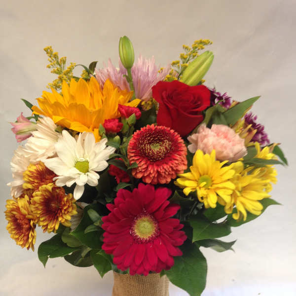 Mixed bouquet with sunflowers, roses, and daisies in a burlap-wrapped vase
