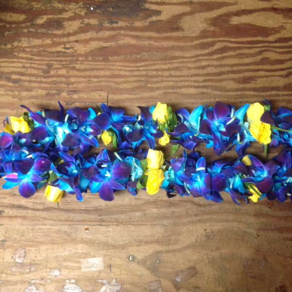 Blue and purple flower lei with yellow rose accents on a wooden surface