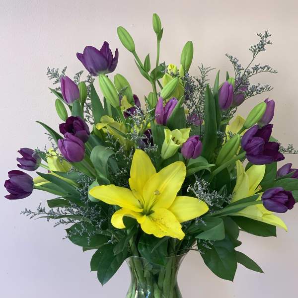 Bouquet of yellow lilies and purple tulips in a clear glass vase