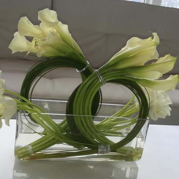 White calla lilies and white tulips arranged in a clear rectangular vase.