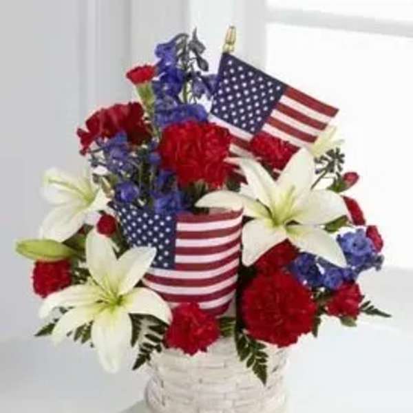 Red, white, and blue floral arrangement in a white basket with American flags