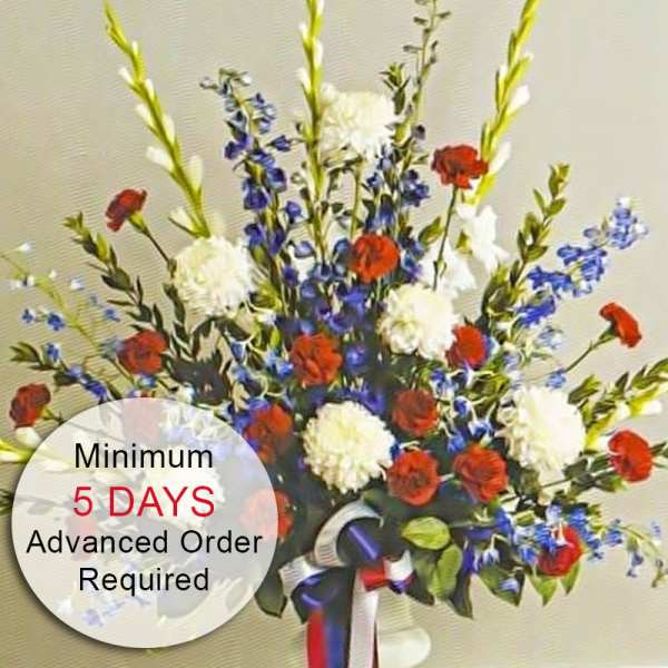 Tall red, white, and blue flower arrangement in a white vase with patriotic ribbon bow