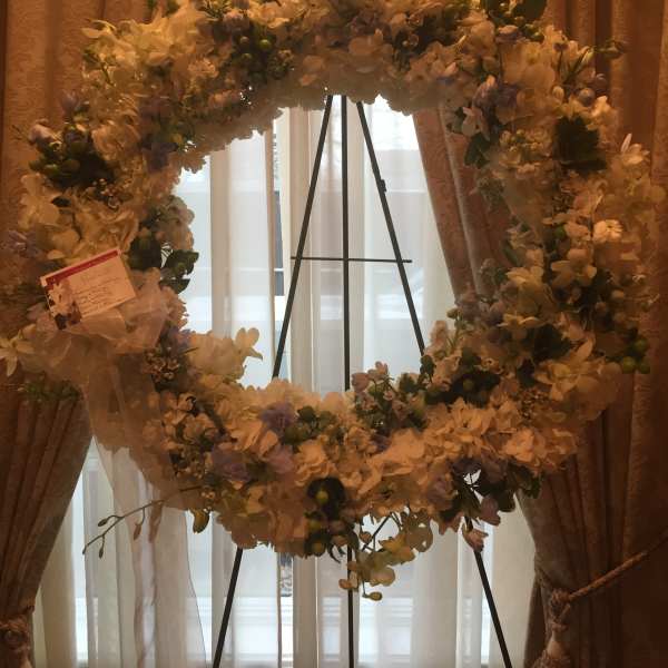 Large white floral wreath on a black stand with a ribbon bow