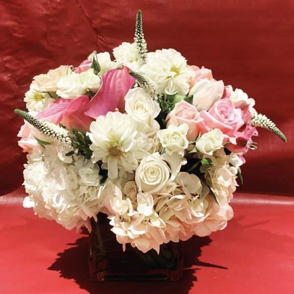 Pink and white floral arrangement in a dark vase on a red background