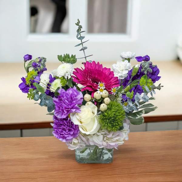 Mixed bouquet in a square glass vase with purple, white, and pink flowers
