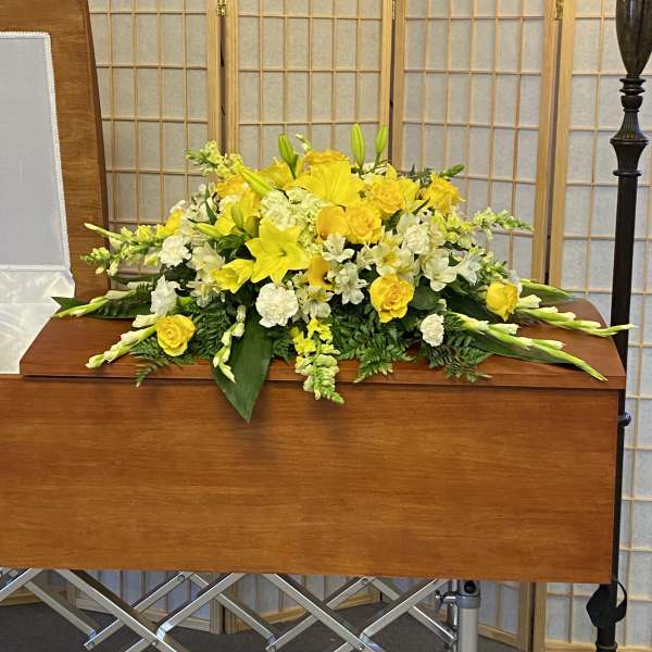Yellow and white floral casket spray on a wooden casket