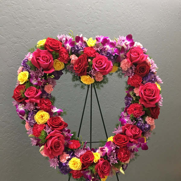 Heart-shaped floral wreath on a stand with red, pink, yellow, and purple flowers