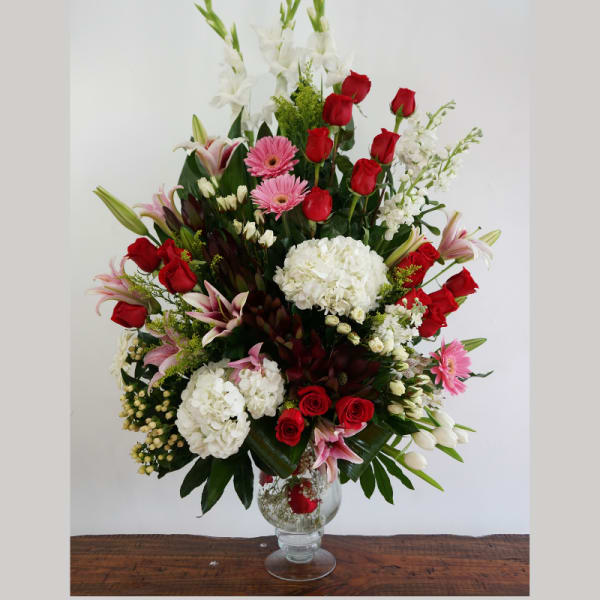 Tall mixed arrangement of red roses, white hydrangeas, pink lilies and gerberas in a clear glass vase