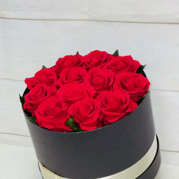 Round black box filled with red roses and wrapped with a cream ribbon