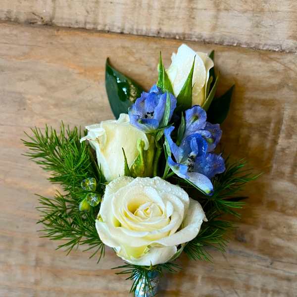 White rose boutonniere with blue flowers and greenery
