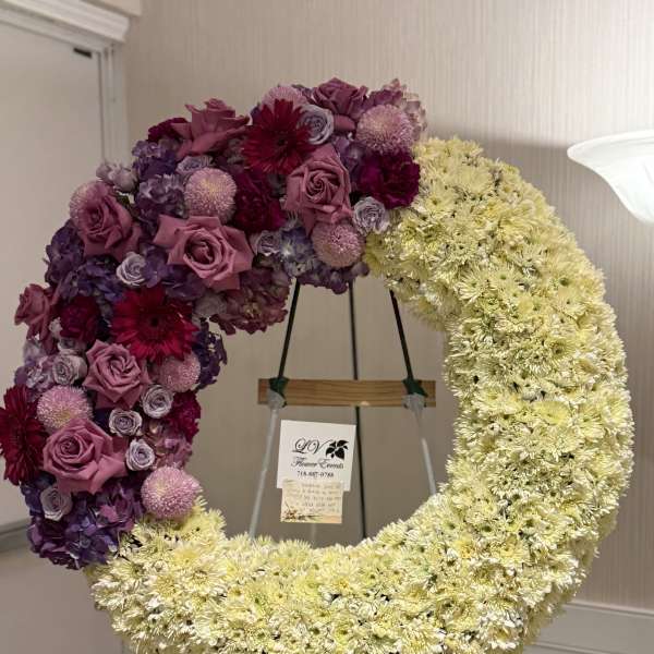 Large crescent floral wreath on an easel with purple, pink, and cream flowers