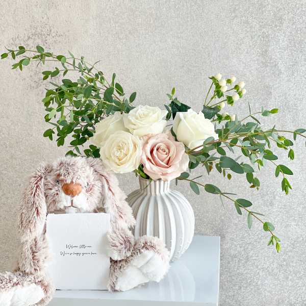 White and blush roses in a ribbed vase with a plush bunny and card