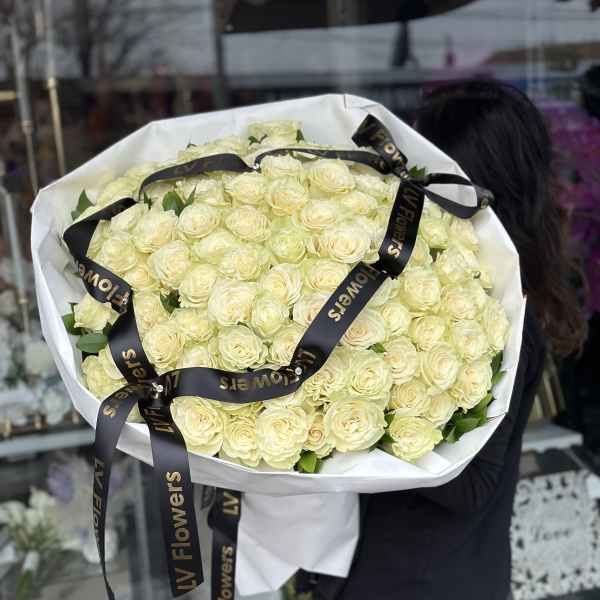 Large bouquet of pale cream roses wrapped in white paper with black ribbon