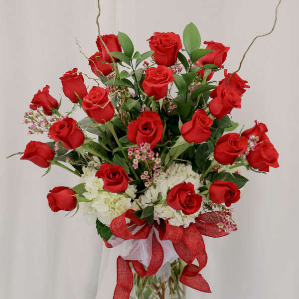 Red roses and white hydrangeas arranged in a glass vase with a red ribbon.