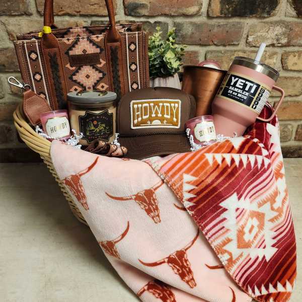 Gift basket with a patterned tote, tumblers, candles, a cap, and folded blankets