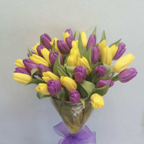 Bouquet of yellow and purple tulips in a clear glass vase with a purple ribbon
