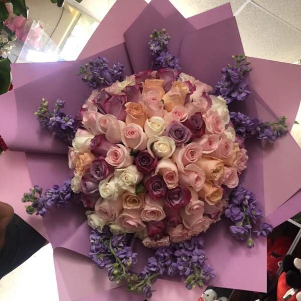 Large bouquet of pastel roses wrapped in pink paper with purple accents