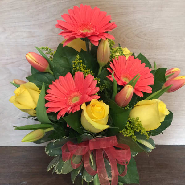 Bouquet of pink gerbera daisies and yellow roses in a glass vase with a red ribbon