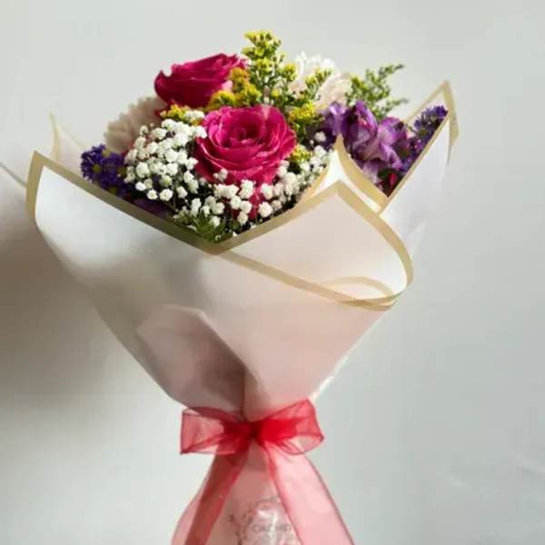 Bouquet of pink roses, purple flowers, and white filler wrapped in paper with a red ribbon