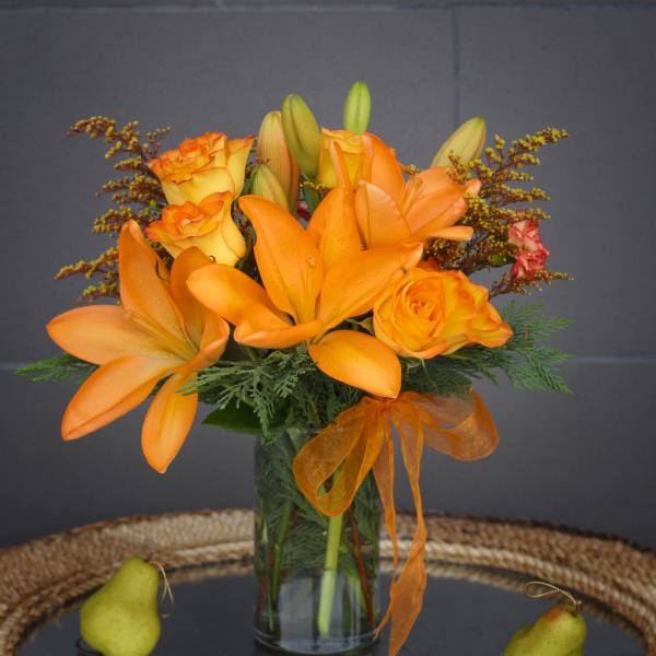 Orange lilies and roses in a glass vase with pears on a tray