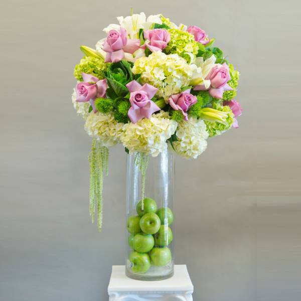Pink roses and white hydrangeas in a tall glass vase with green apples