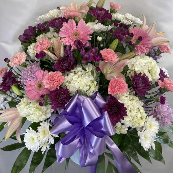 Pink and white mixed flower arrangement with a purple ribbon bow