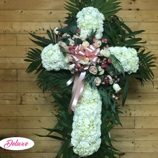 White floral cross arrangement with pink roses and ribbon on a wooden wall