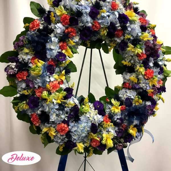 Large floral wreath on a stand with blue, purple, yellow, and coral flowers